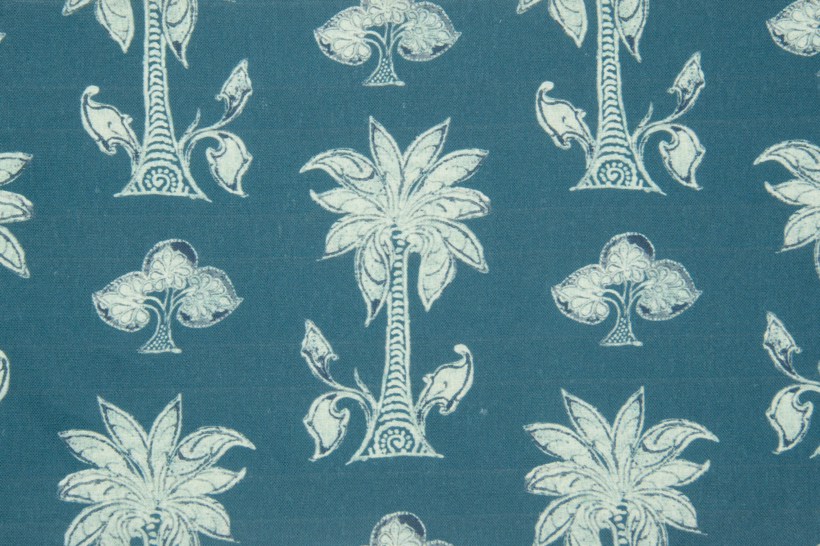 Detail of fabric in a playful palm tree print in white and navy on a blue field.