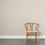 A wooden chair stands in front of a wall papered in a repeating leaf print in white on a cream field.