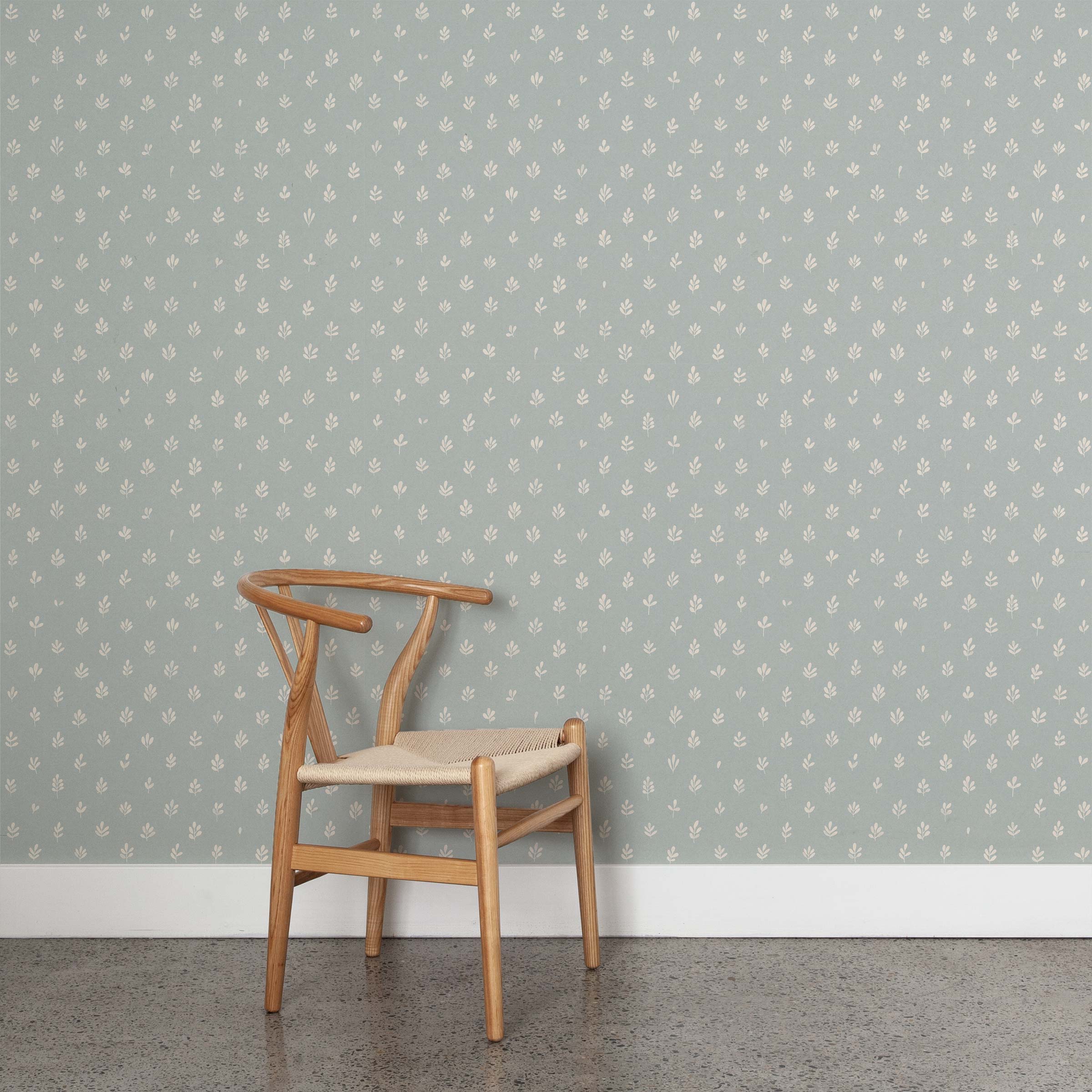 A wooden chair stands in front of a wall papered in a repeating leaf print in cream on a light blue field.