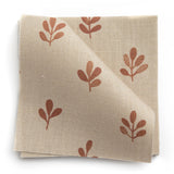 A stack of fabric swatches in a repeating leaf print in burnt orange on a cream field.