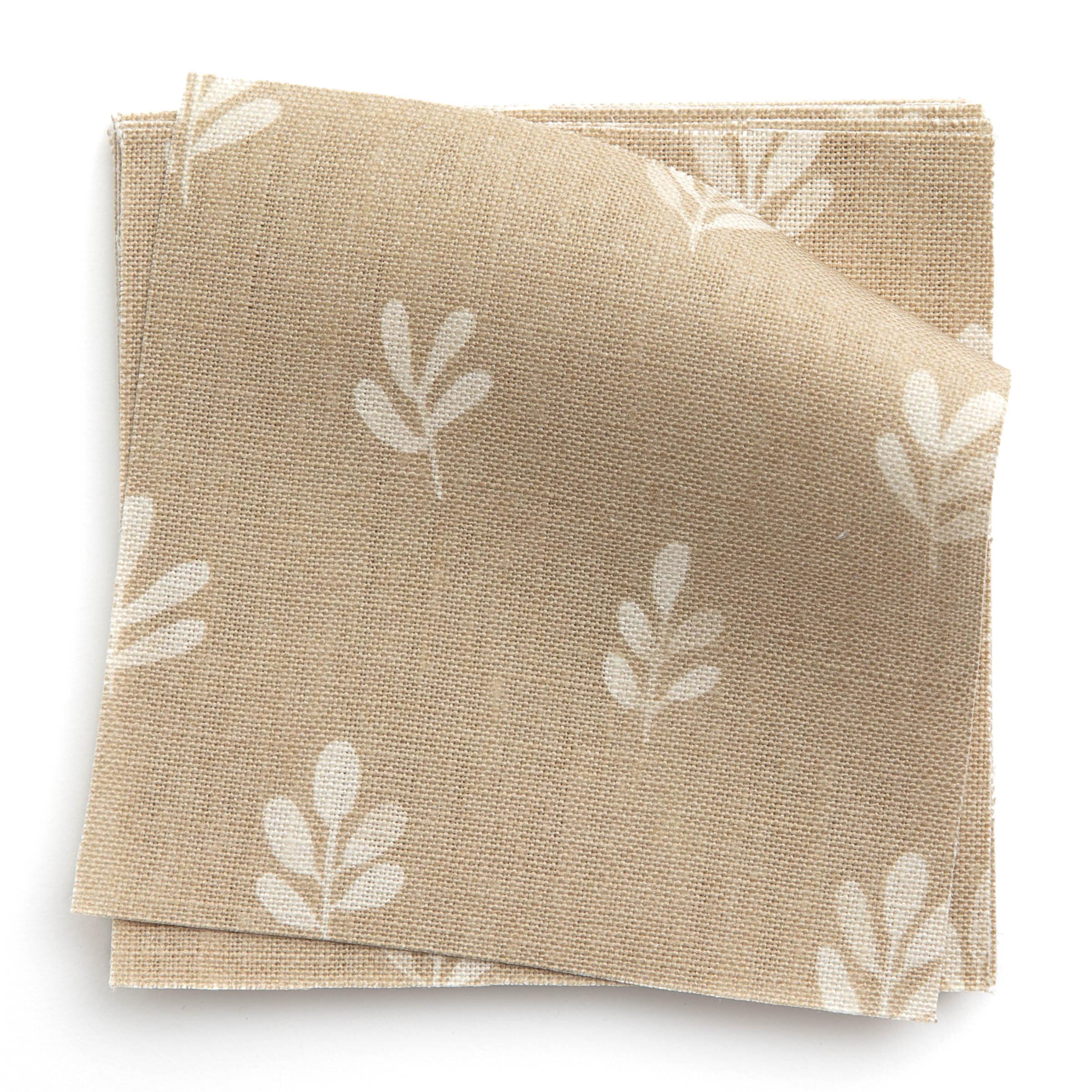 A stack of fabric swatches in a repeating leaf print in cream on a tan field.