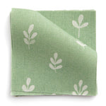 A stack of fabric swatches in a repeating leaf print in cream on a green field.