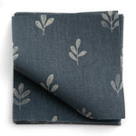 A stack of fabric swatches in a repeating leaf print in cream on a navy field.
