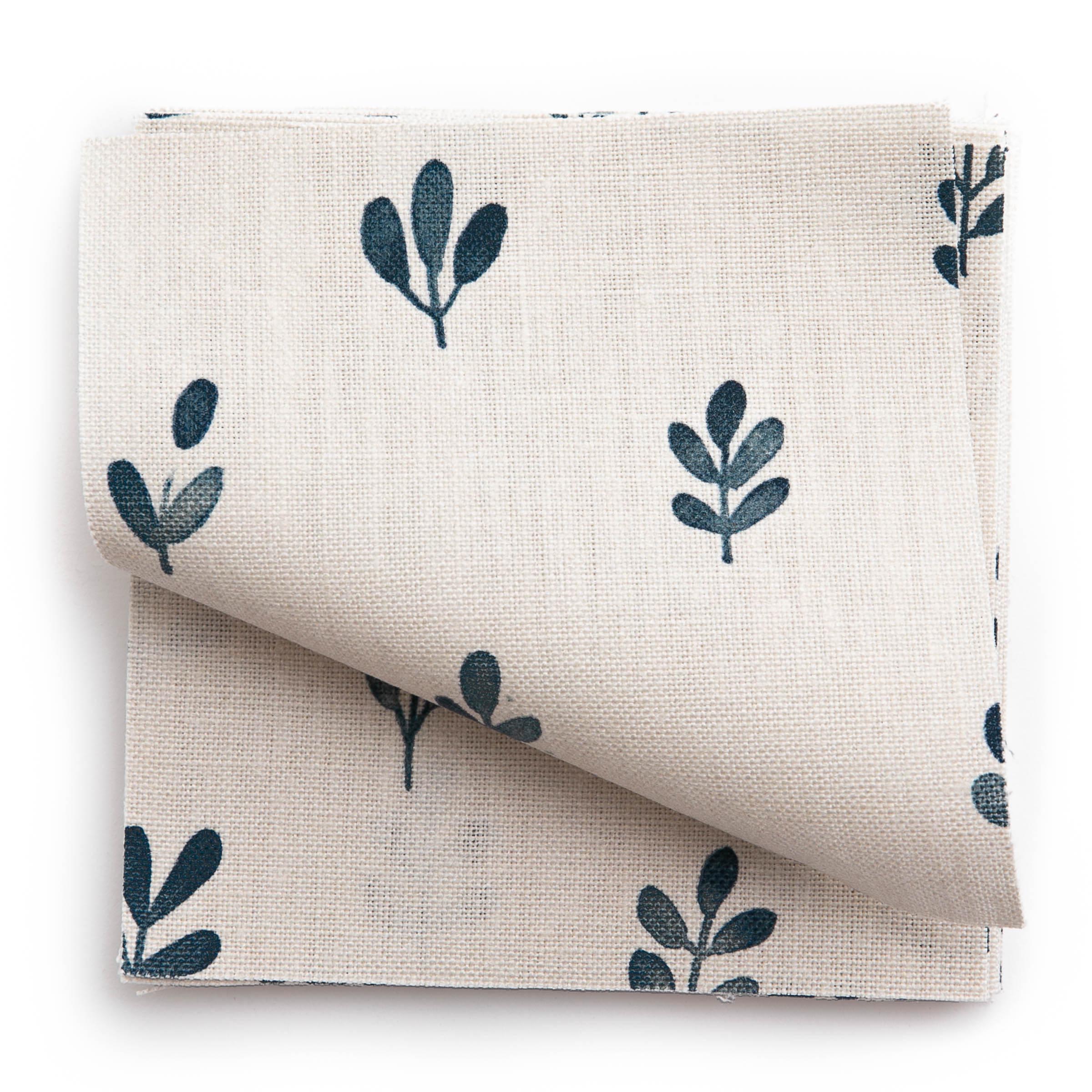 A stack of fabric swatches in a repeating leaf print in navy on a cream field.