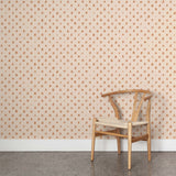 A wooden chair stands in front of a wall papered in a repeating leaf print in burnt orange on a cream field.