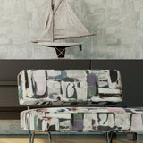 A minimalist armchair upholstered in an abstract layered paint blotch print in gray, white, olive and purple.