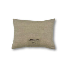 Rectangular throw pillow in solid natural linen with a rectangular tag at bottom center with Lindsay Alker and a leaping ram logo.