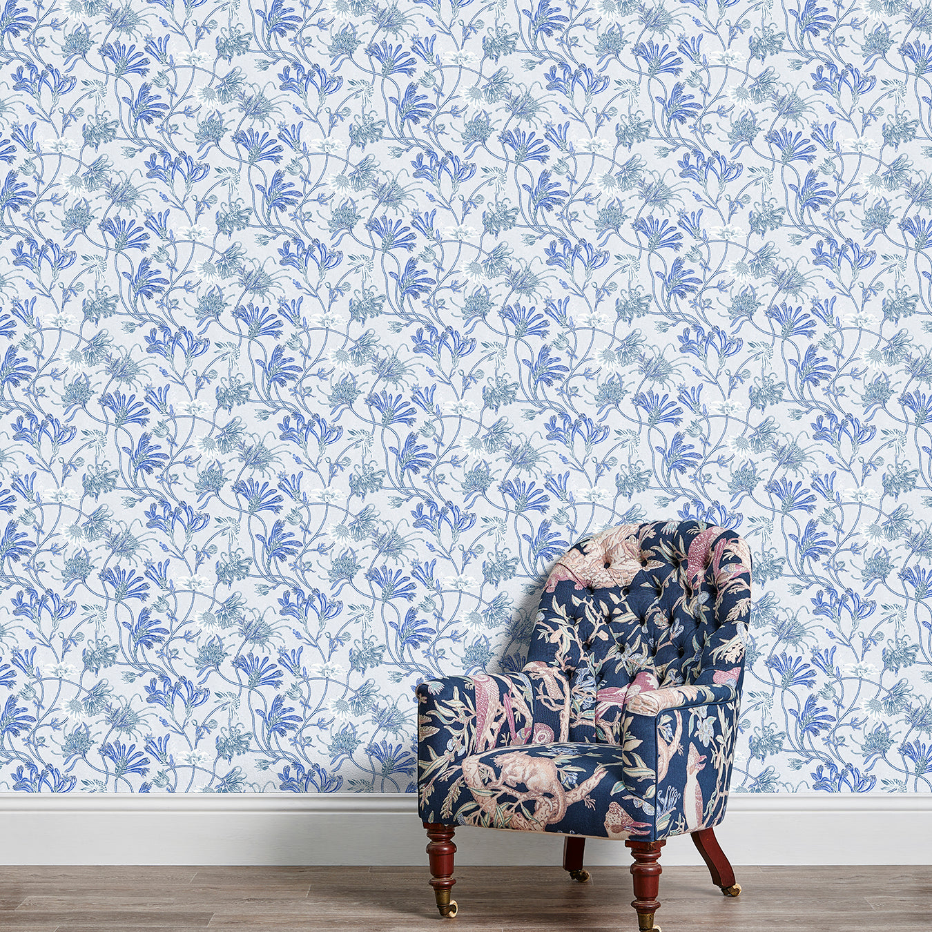 An armchair stands in front of a wall papered in a painterly floral print in white, blue and navy.