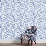 An armchair stands in front of a wall papered in a painterly floral print in white, blue and navy.