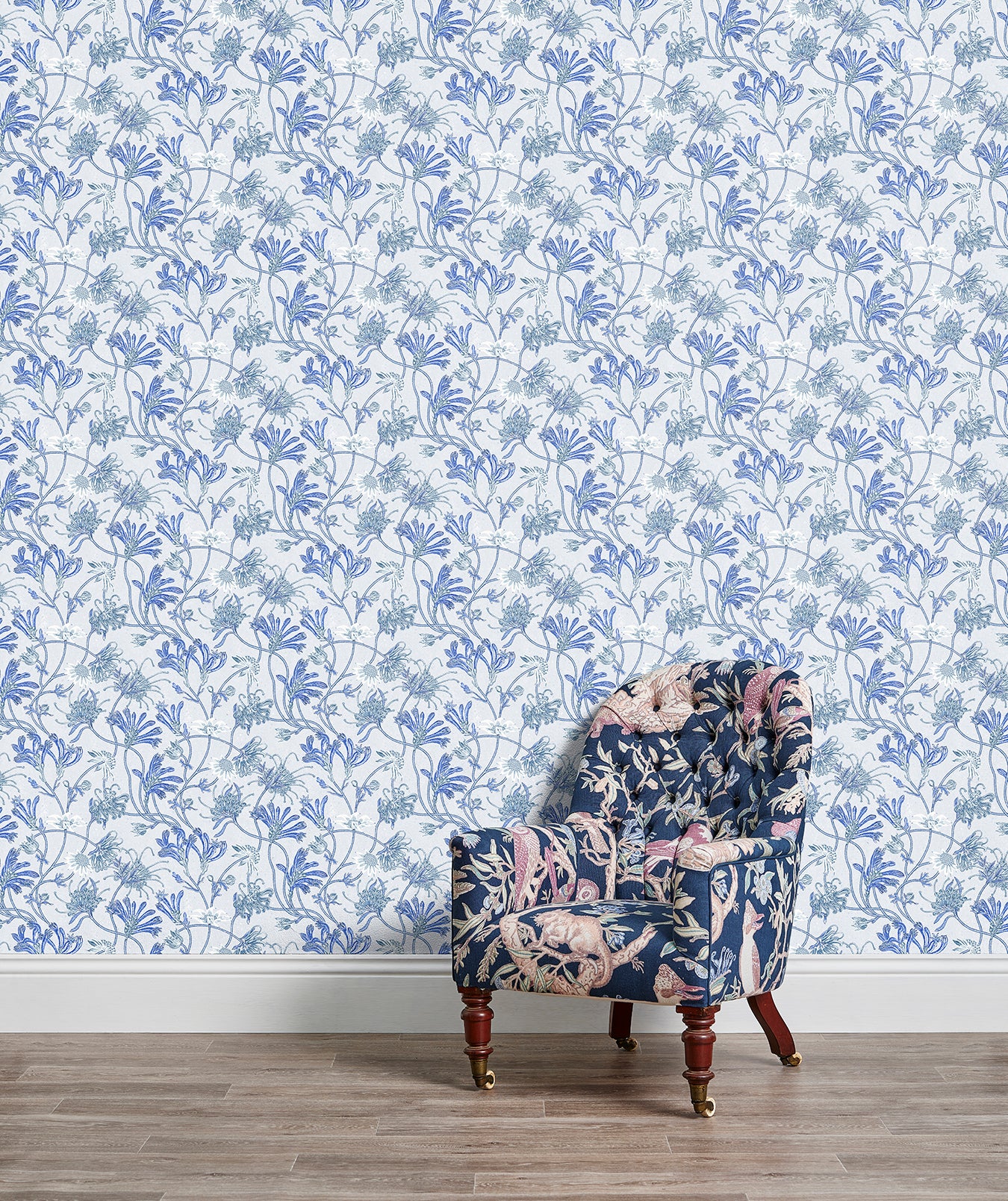 An armchair stands in front of a wall papered in a painterly floral print in white, blue and navy.