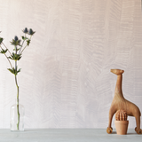 A table with knick knacks stands in front of a wall papered in an abstract textural pattern in metallic and blush.