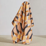 A large piece of draped fabric in a striped triangle print in shades of orange, purple, peach and cream.