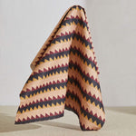 A large piece of draped fabric in a striped triangle print in shades of peach, maroon and black.