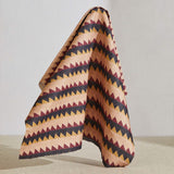 A large piece of draped fabric in a striped triangle print in shades of peach, maroon and black.