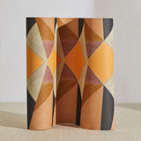 A curved partition stands on the ground, covered in a large-scale triangle print in shades of orange, tan, pink and gray.