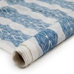 Partially unrolled fabric in an intricate diamond stripe print in blue and navy on a cream field.