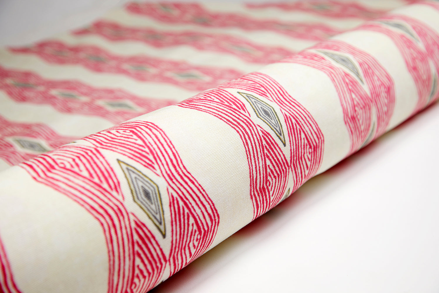 Partially unrolled fabric in an intricate diamond stripe print in pink and green on a cream field.