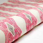 Partially unrolled fabric in an intricate diamond stripe print in pink and green on a cream field.