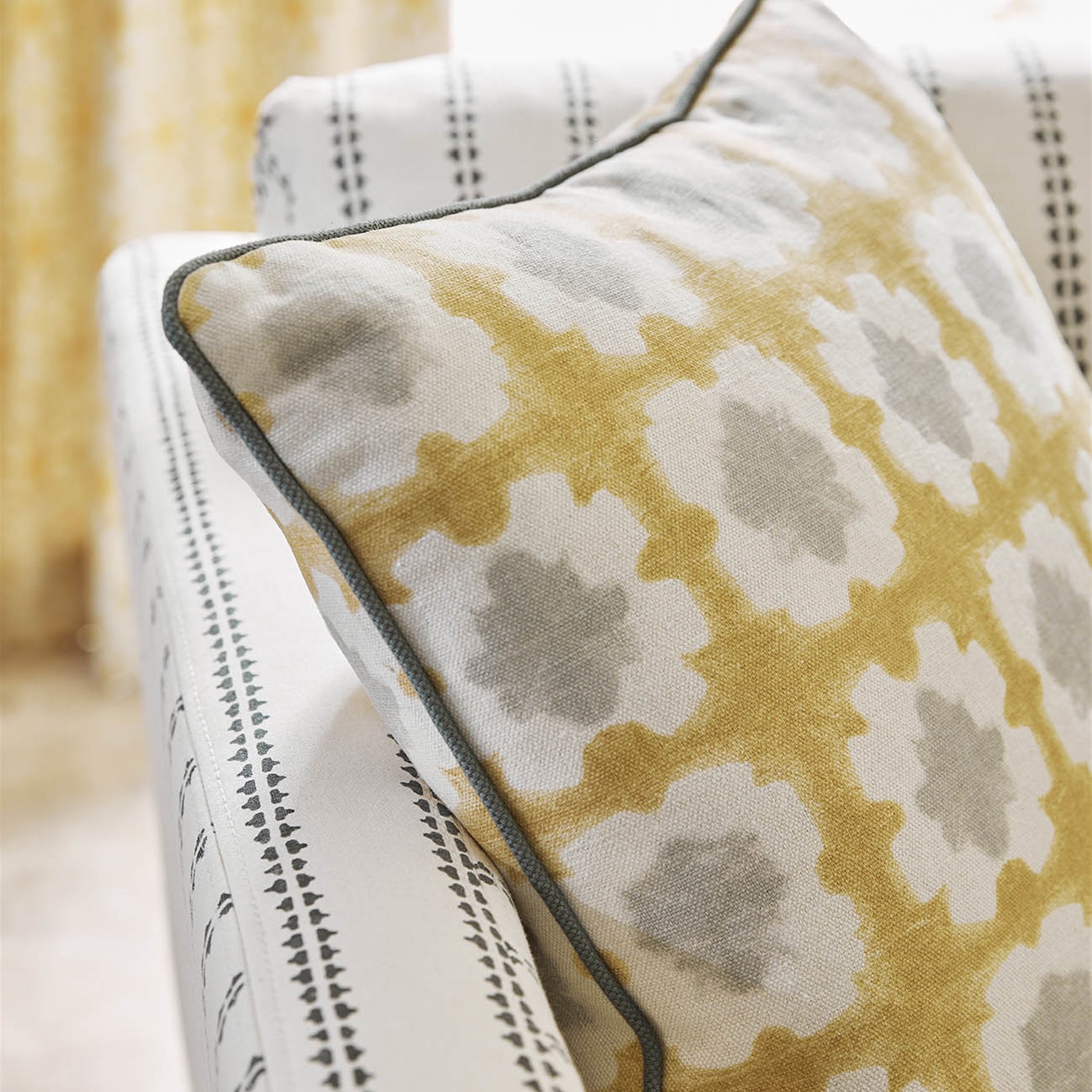 Close-up of a throw pillow upholstered in a dyed grid print in yellow, gray and cream.