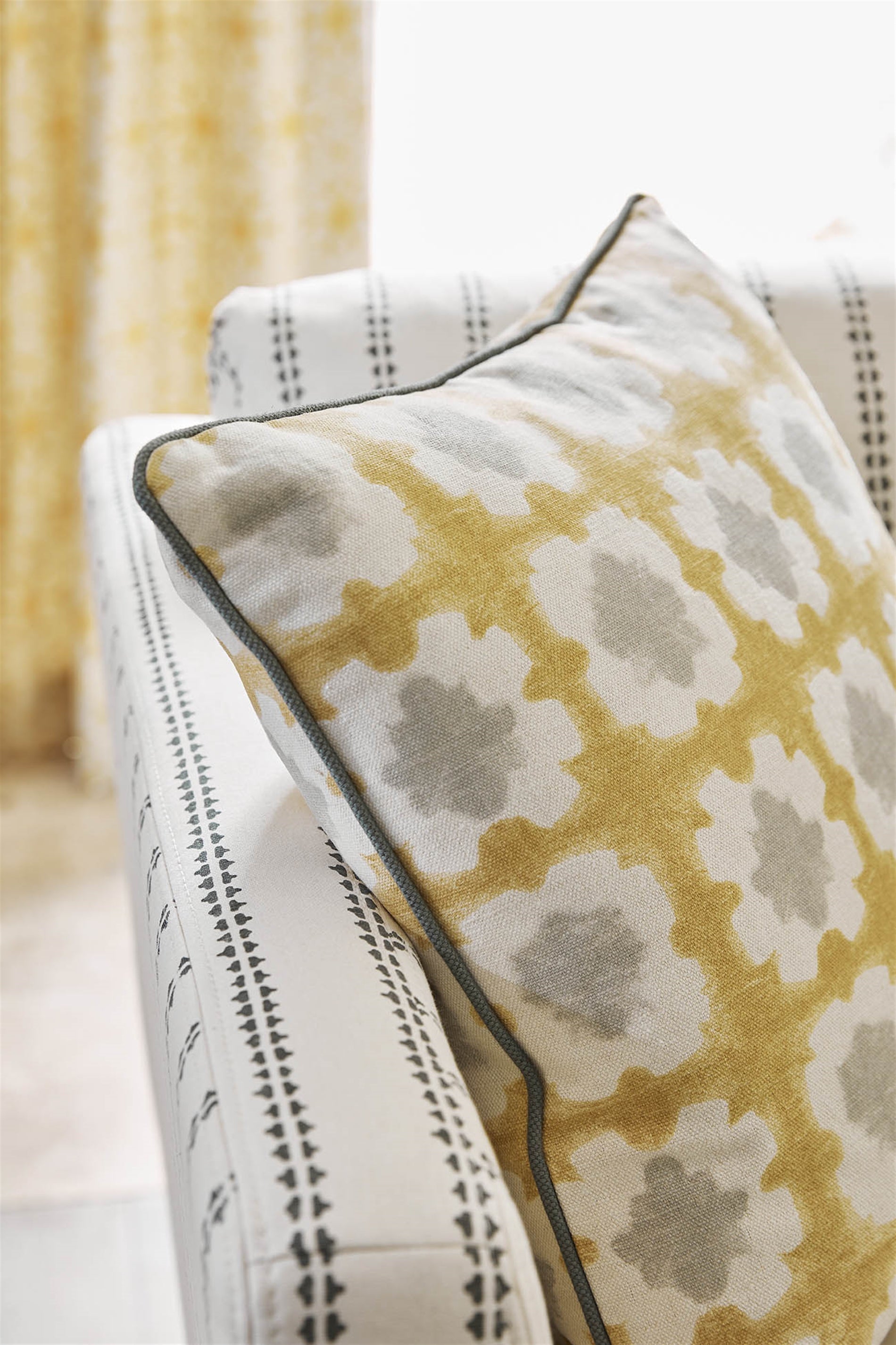 Close-up of a throw pillow upholstered in a dyed grid print in yellow, gray and cream.