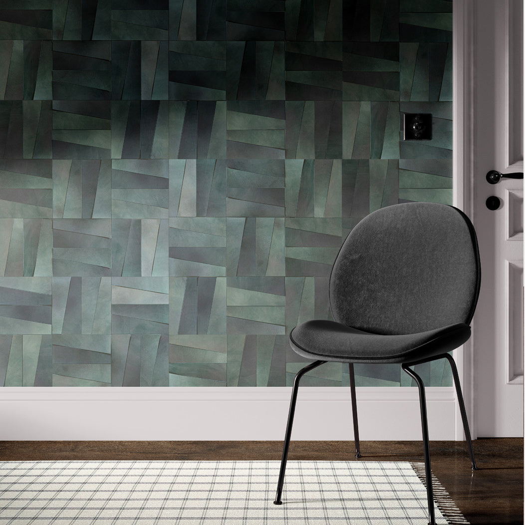 A gray arm chair stands in front of a wall papered in leather wall tiles in a repeating geometric pattern.