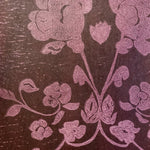 Detail of wallpaper in a repeating floral damask pattern in pink on a brown field.