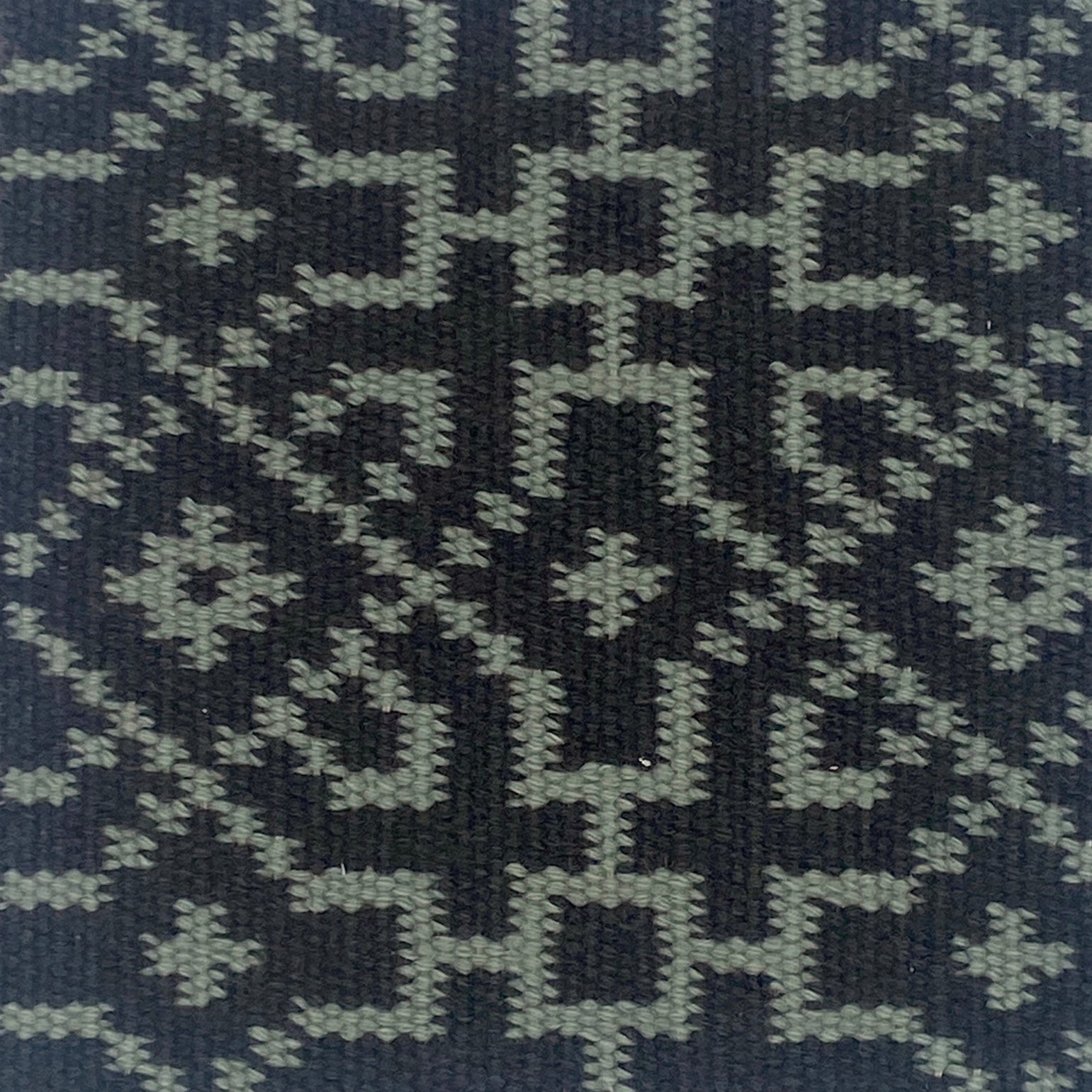Close-up of a textured rug with a geometric pattern in turquoise on black