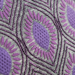 Detail of fabric with a dimensional floral medallion pattern embroidered in shades of purple on a gray field.