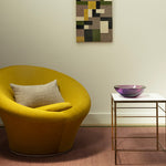 Yellow chair with a textured pillow in a room with a abstract patterned wall art.