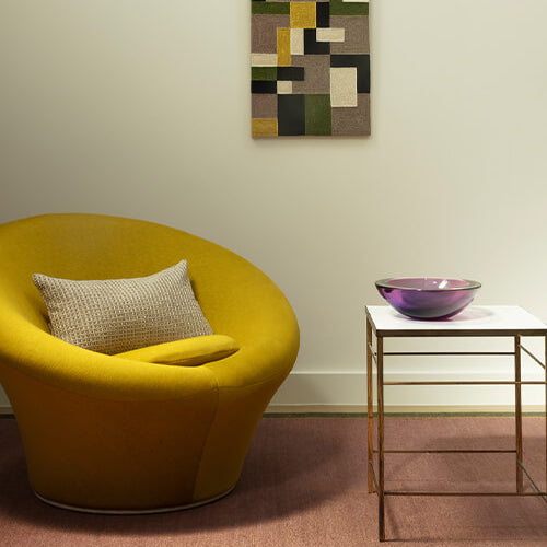 Yellow chair with a textured pillow in a room with a abstract patterned wall art.