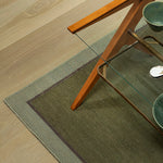 Green rug on a wooden floor with a glass table and wooden chair.