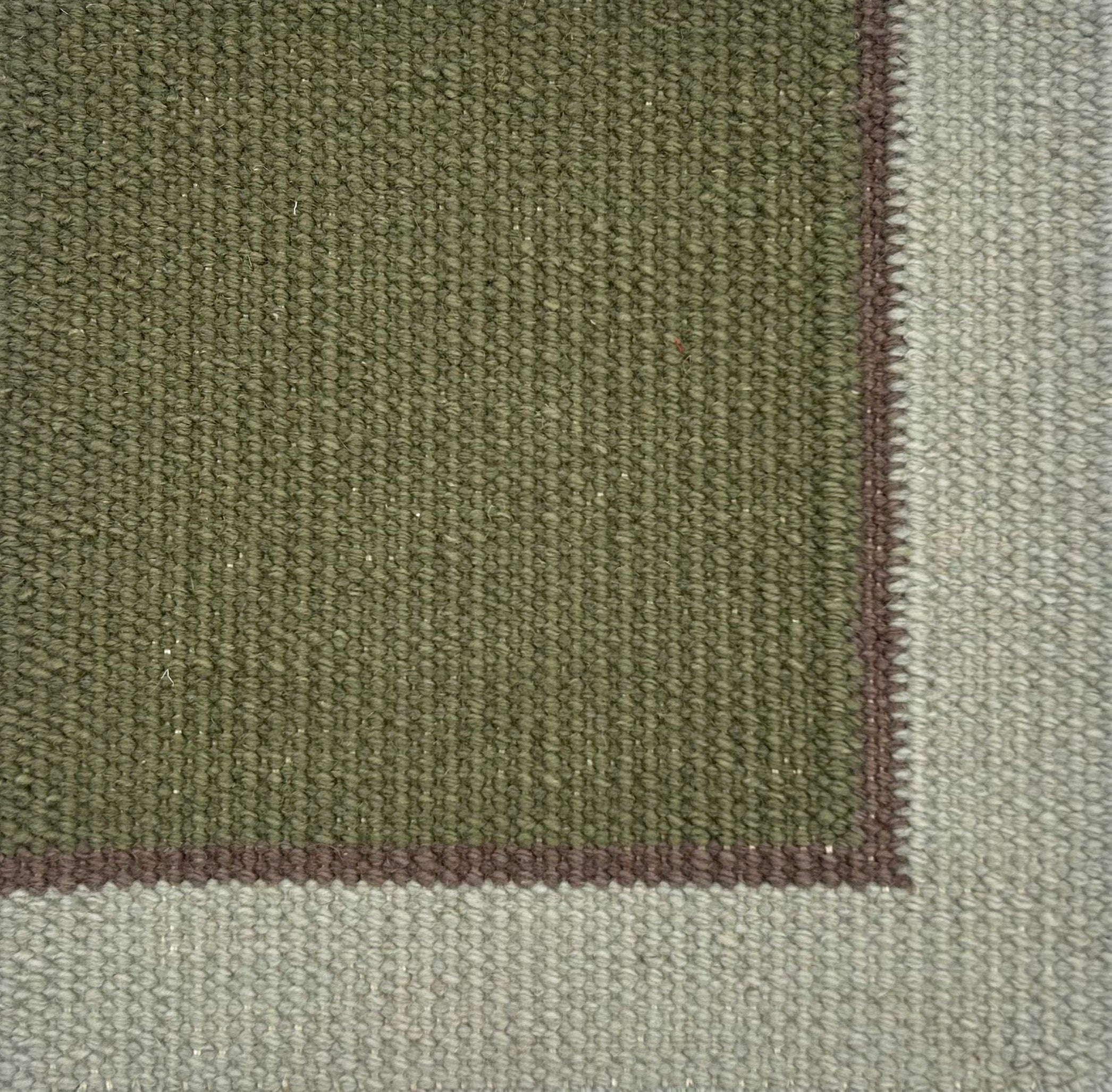 Close up of a flatweave rug in green with a brown and grey border. 