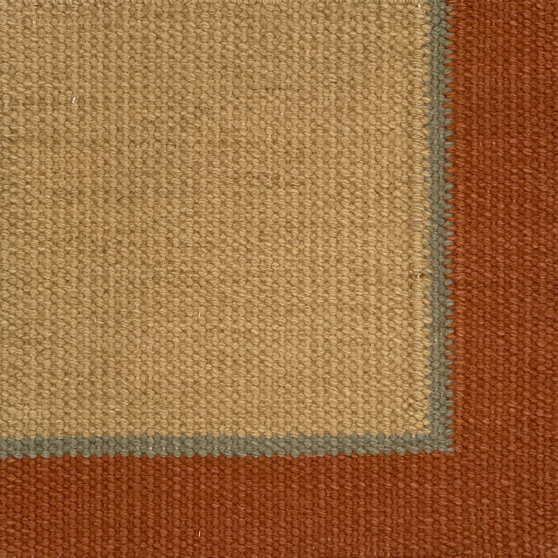 Close up of a flatweave rug in tan with a blue and coral border. 