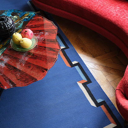Living room scheme with curved red couch and sculptural coffee table over a a flatwoven rug in a geometric border in blue, black, red and cream.