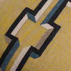 Detail of fabric with a stripe of geometric embroidery in shades of black, blue and gray on a gold field.