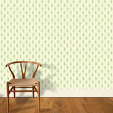 A wooden chair stands in front of a wall papered in a floral paisley print in green on a light yellow field.