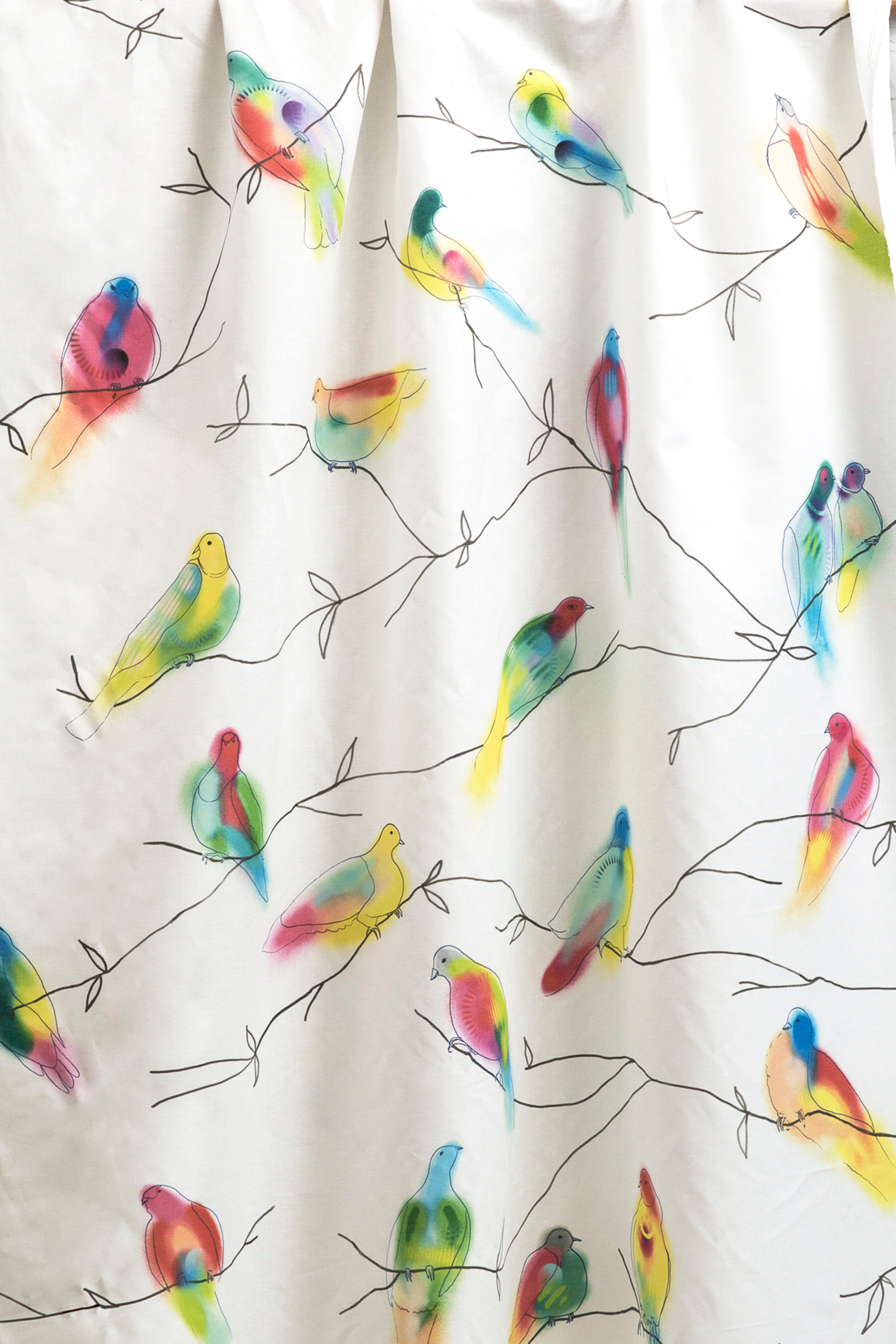 Draped fabric yardage in a painterly bird and branch print in green, yellow, pink and black on a white field.