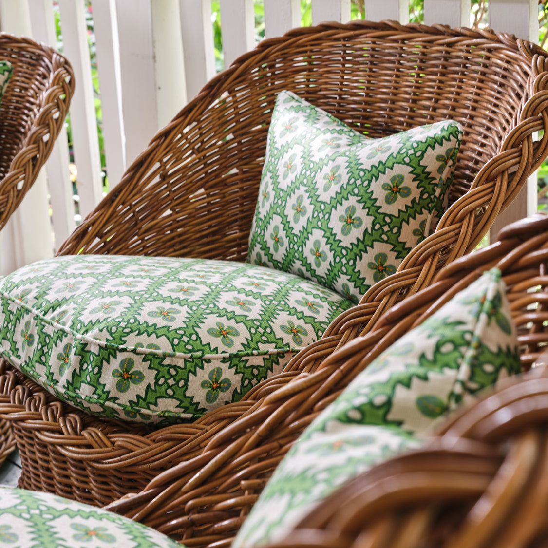 A cluster of wicker armchairs with cushions upholstered in a playful floral grid print in green, orange and white.