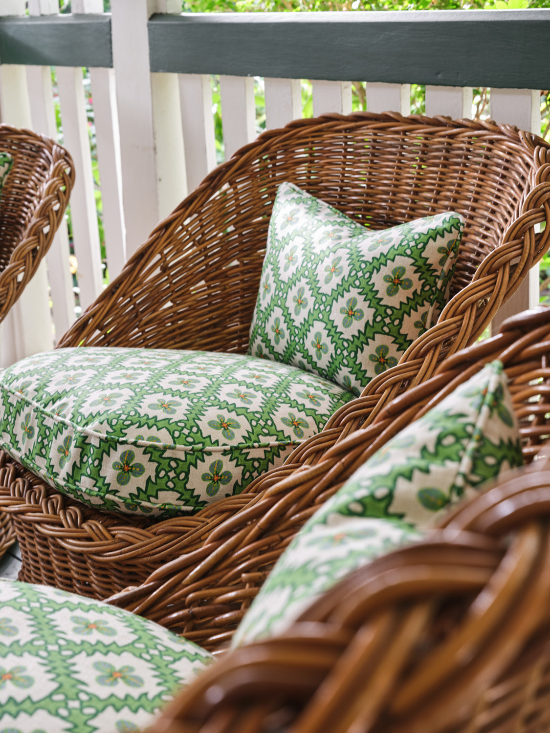 A cluster of wicker armchairs with cushions upholstered in a playful floral grid print in green, orange and white.