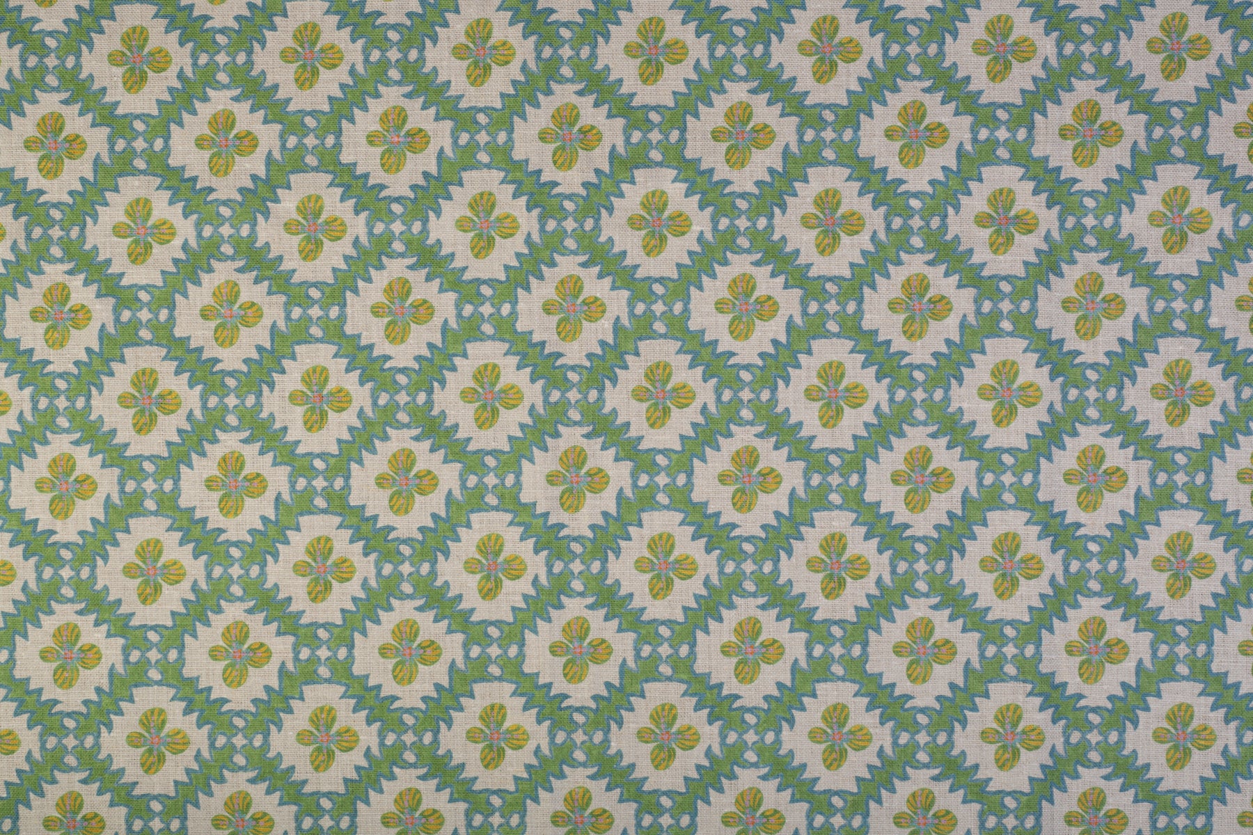 Detail of fabric in a playful floral grid print in green, yellow and blue on a white field.