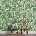 Two wooden chairs stand in front of a wall papered in a dense bird and botanical print in orange, pink and green.