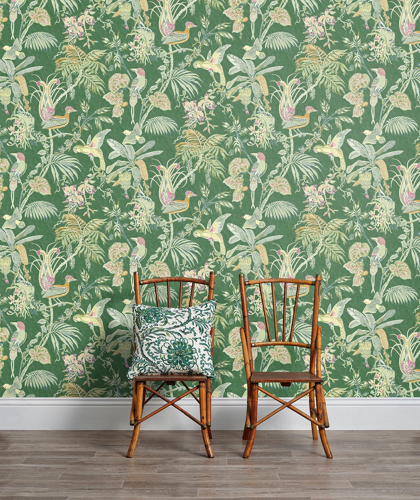 Two wooden chairs stand in front of a wall papered in a dense bird and botanical print in orange, pink and green.