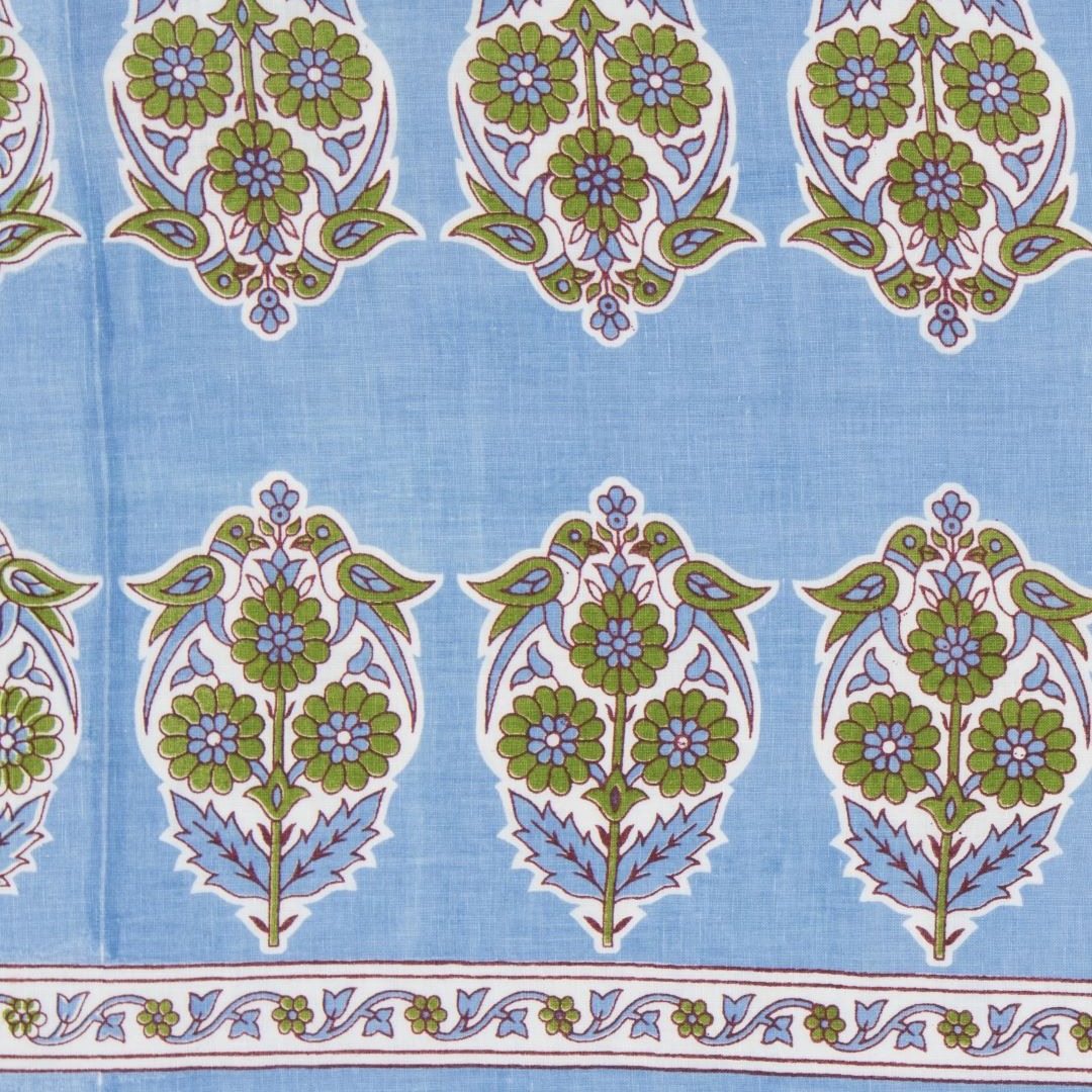 Detail of fabric in a repeating bird and floral paisley in green, white and blue on a blue field.