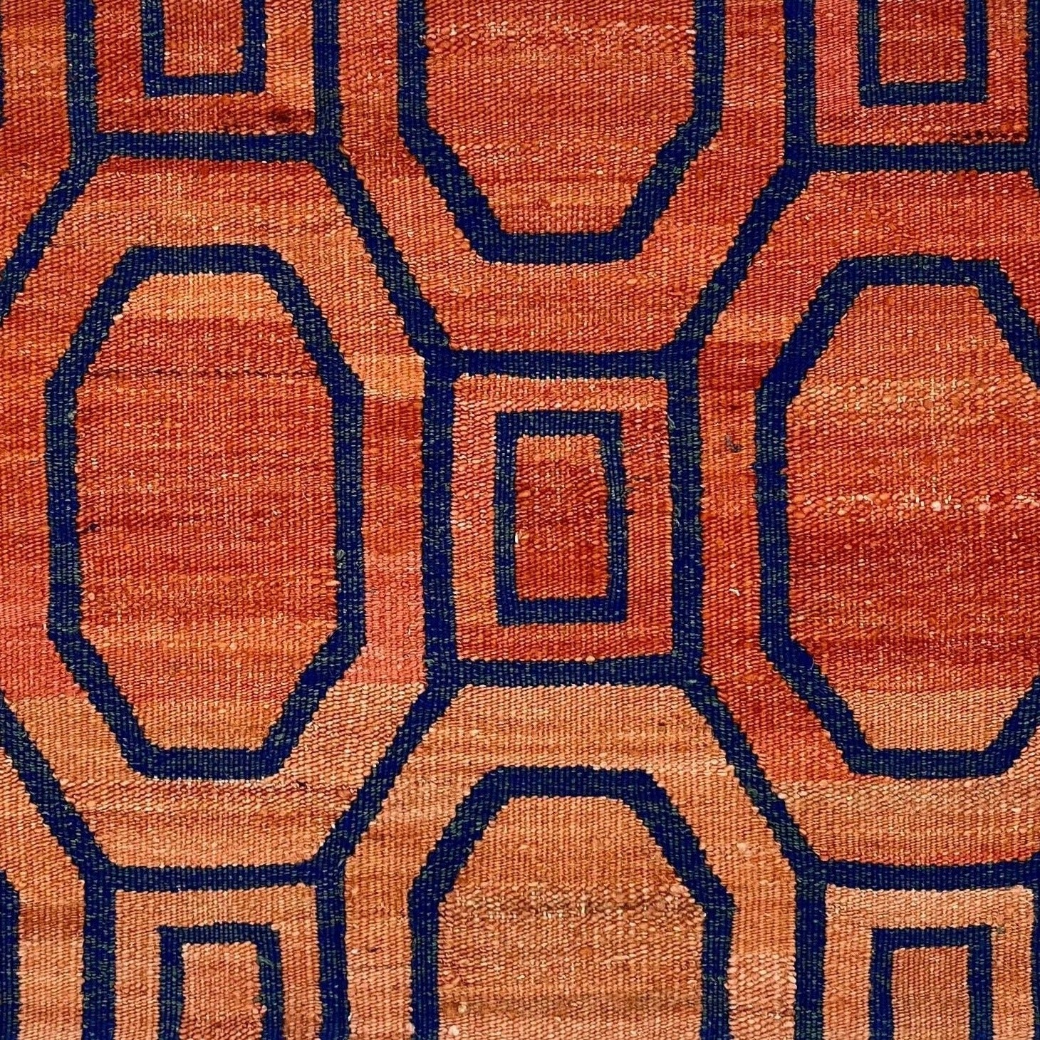 A flatweave rug with a melange of light orange to darker orange and a dark blue contemporary lattice pattern.