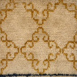 Handknotted rug sample with an ochre filigree design on a beige field.