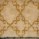 Handknotted rug sample with an ochre filigree design on a beige field.