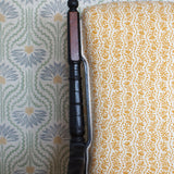 Wooden chair with a yellow floral fabric against wallpaper in a pastel floral pattern.