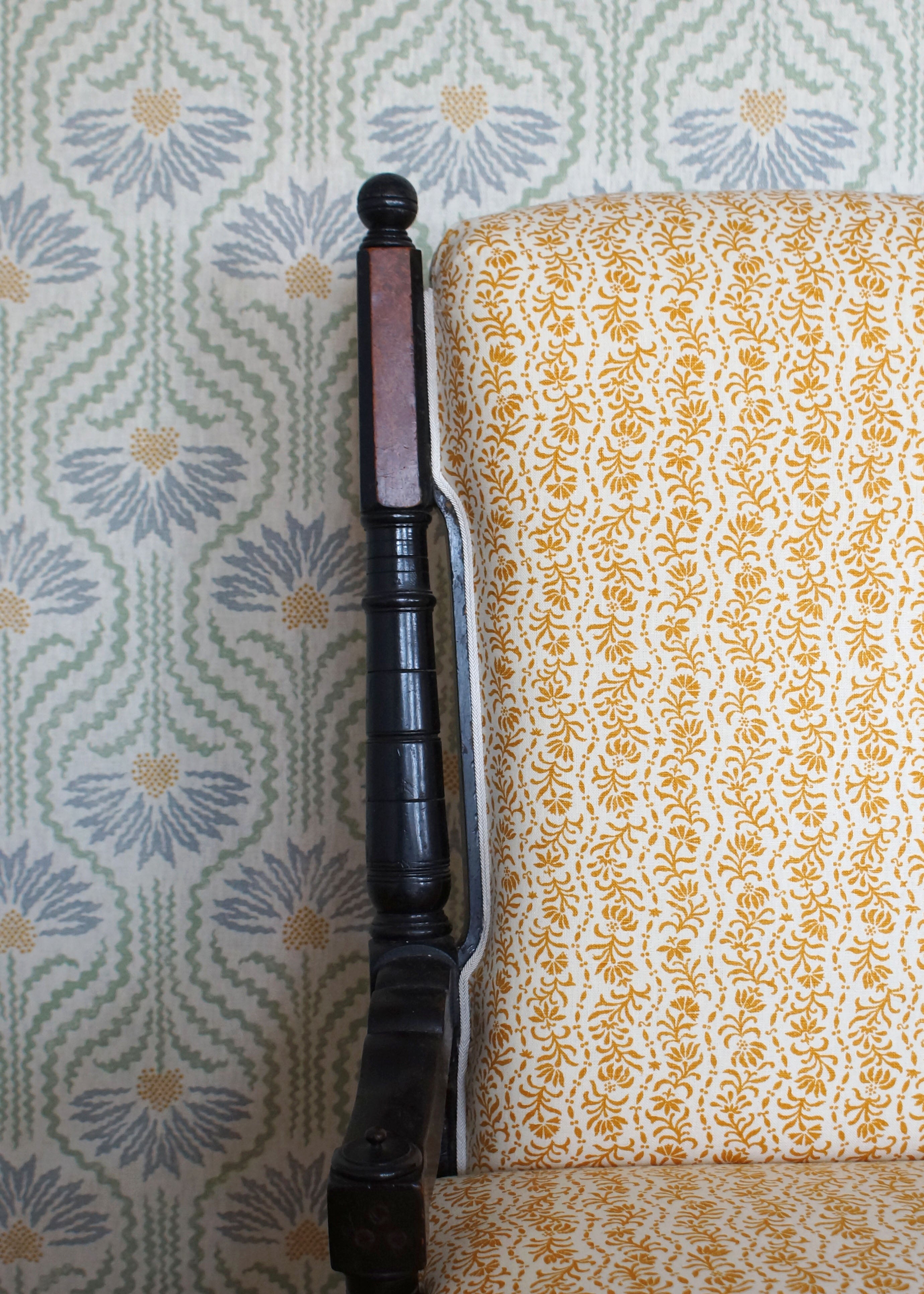 Wooden chair with a yellow floral fabric against wallpaper in a pastel floral pattern.
