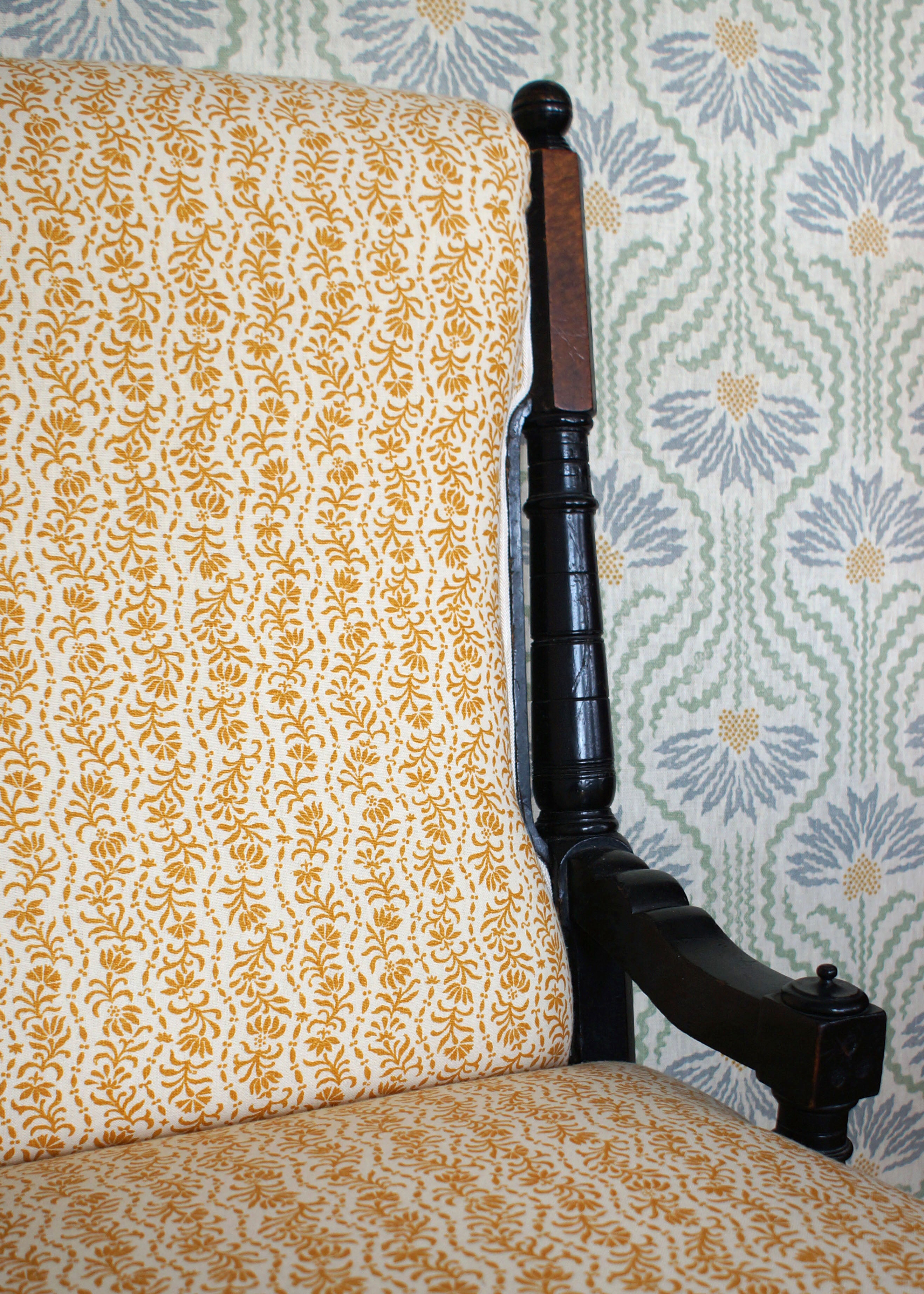 Chair with yellow floral patterned fabric against a floral wallpaper background