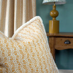 Decorative pillow with floral pattern on a couch, next to a lamp and curtain.